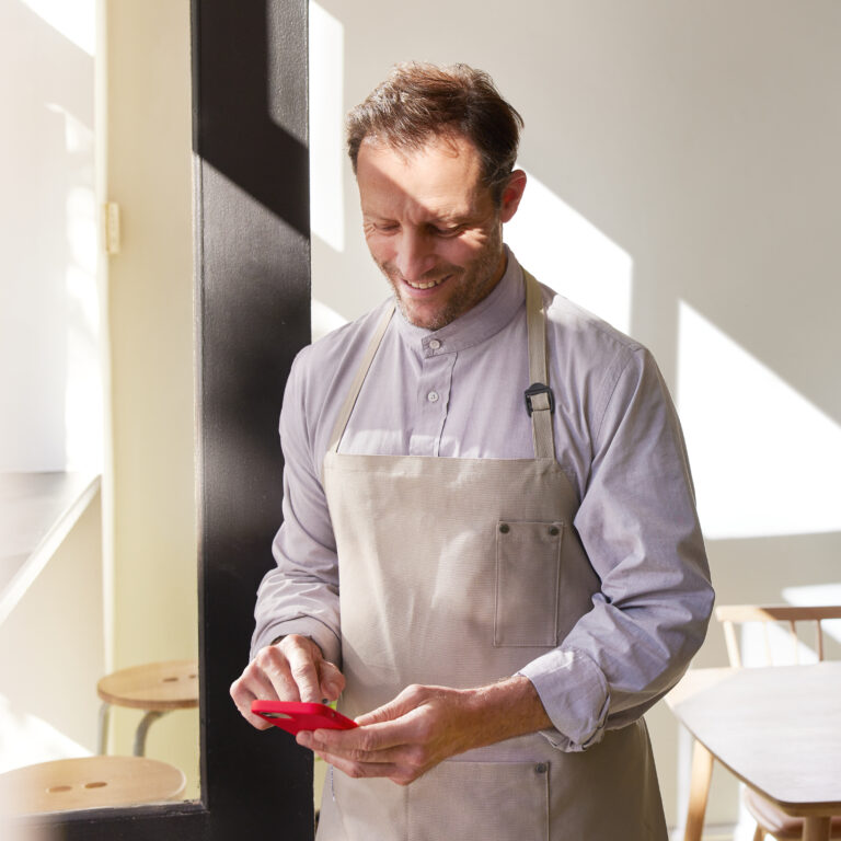 Worker wearing apron looking at his phone